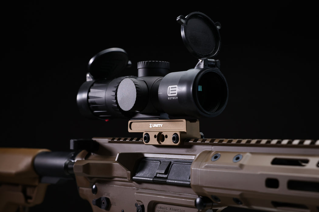 An isometric lifestyle shot of a Cobalt Kinetics rifle featuring the Flat Dark Earth FAST Kickr mount securing a Vudu scope, showcasing the color-matched setup and streamlined 1.54-inch profile in a field environment.