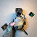 A gloved hand holds a folded coyote brown 3M Peltor ComTac headset, displaying the exterior earcup branding and the integrated downlead cable used to establish secure battle comms in tactical environments.