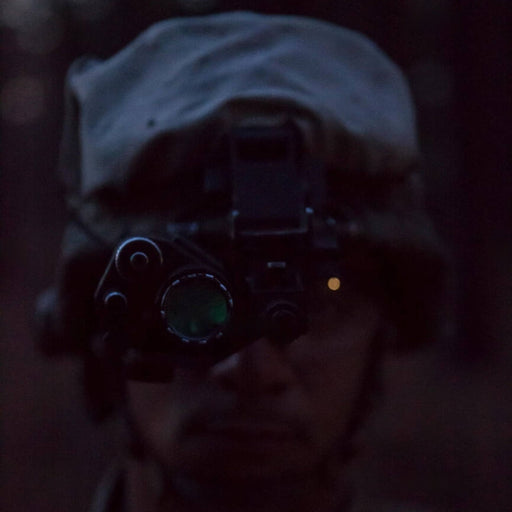 A detailed frontal view of the pvs 14 tube featuring a green Photonis phosphor image, highlighting the diopter focus ring and battery compartment cap in the foreground.