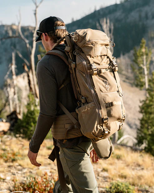 Hiker Kurtis stands on a mountain ridge wearing the Eberlestock Brute 3500 60L Pack, demonstrating how the internal frame and vapor-series components provide a stable, balanced carry during steep ascents.