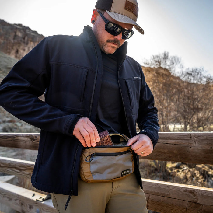 A hiker stowing his wallet in the Coyote Brown Eberlestock Bando XL, demonstrating the ample storage space available for personal items on the trail.