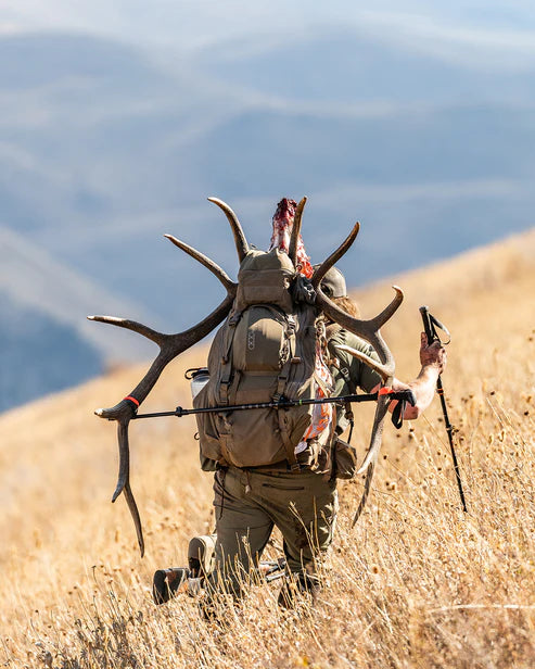 A determined hunter treks through rugged terrain during a 2025 elk hunt, using his Dry Earth Brute 6500 Meat Hauler to carry a heavy harvest with stability and ease.