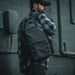 man wearing grey flannel shirt and black cap carries vertx urban ghost backpack on right shoulder