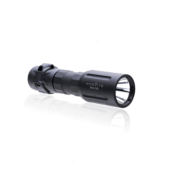 An image of the modlite FUEL 18350 flashlight showcasing the item on its isometric view and the black tactical flashlight in the middle of the photo and with a textured grip and white product lettering detailing its dual fuel capabilities on a reflective surface and with the gascap attached to it.