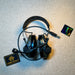 An olive drab green tactical ballistic headset stands upright on a textured surface, displaying its flexible boom microphone and adjustable headband next to an Atomic Defense patch.