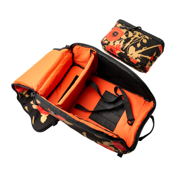 An open otte gear helmet bag featuring a unique black and tan camouflage pattern with bright red poppy flowers, showing a high-visibility orange interior alongside its matching rectangular night vision storage case.
