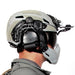 person is shown from the side wearing a kitted-out tactical helmet with a galvion caiman nvg arm visor against a white background