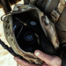 A person wearing a camouflage eberlestock rig looks down into the open main compartment, which securely holds a black Sig Sauer rangefinder and other small tactical tools.