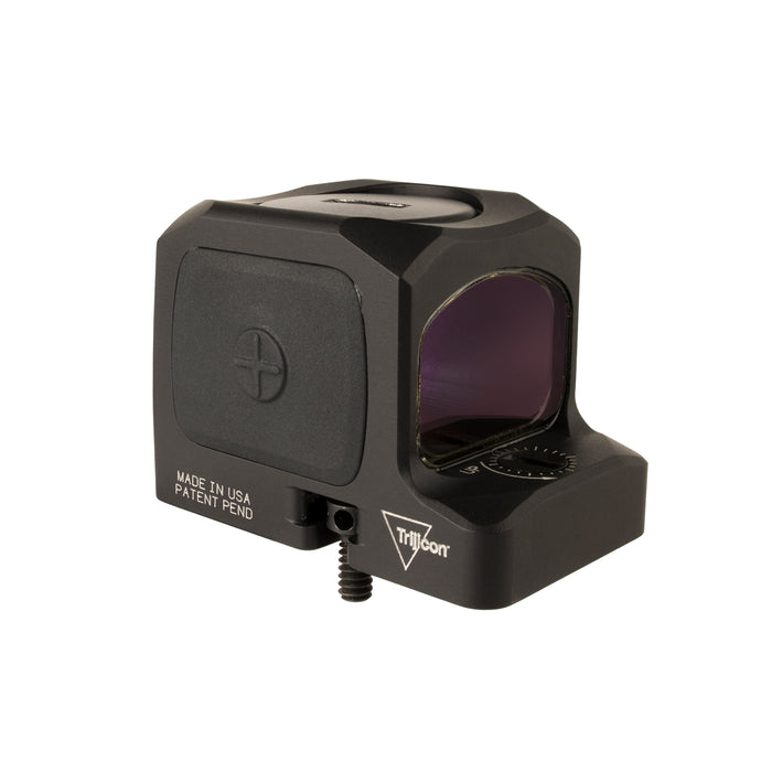 a back isometric product photo of the Trijicon RCR Red Dot Sight against a plain white background and prominently featured at the front-left, reflecting a dramatic green and orange dichroic coating and showing small white laser-engraved markings are visible along the base on the right side and the small Trijicon 'Tri' triangle logo above it.