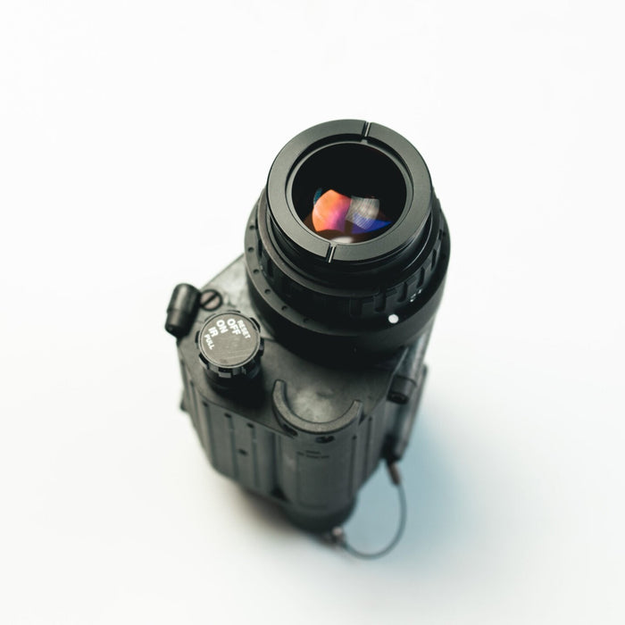 This rear perspective of the pvs 14 night vision goggles clearly displays the objective lens and the rotary on-off power switch in the immediate foreground of the device.