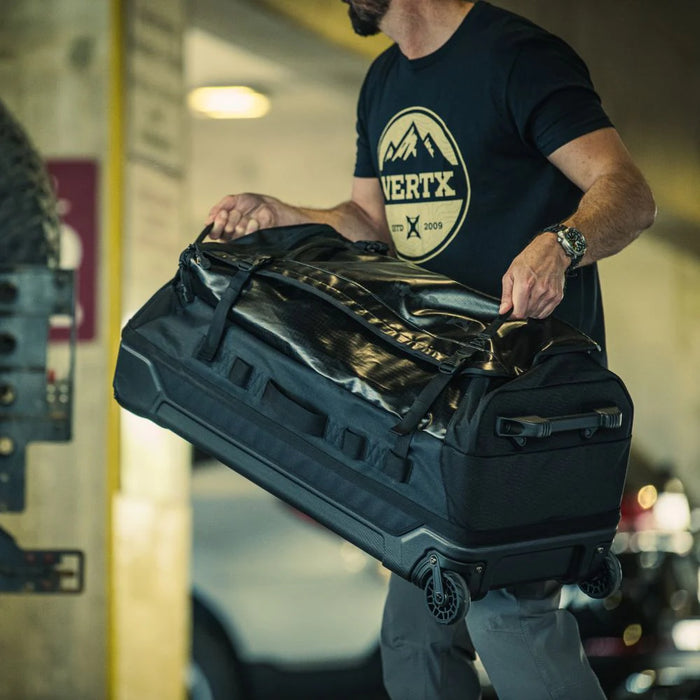 A man is shown loading his RLT 100L Roller Duffel Bag into the back of a truck, utilizing the heavy-duty top and bottom handles to securely lift the large gear hauler into the vehicle bed.