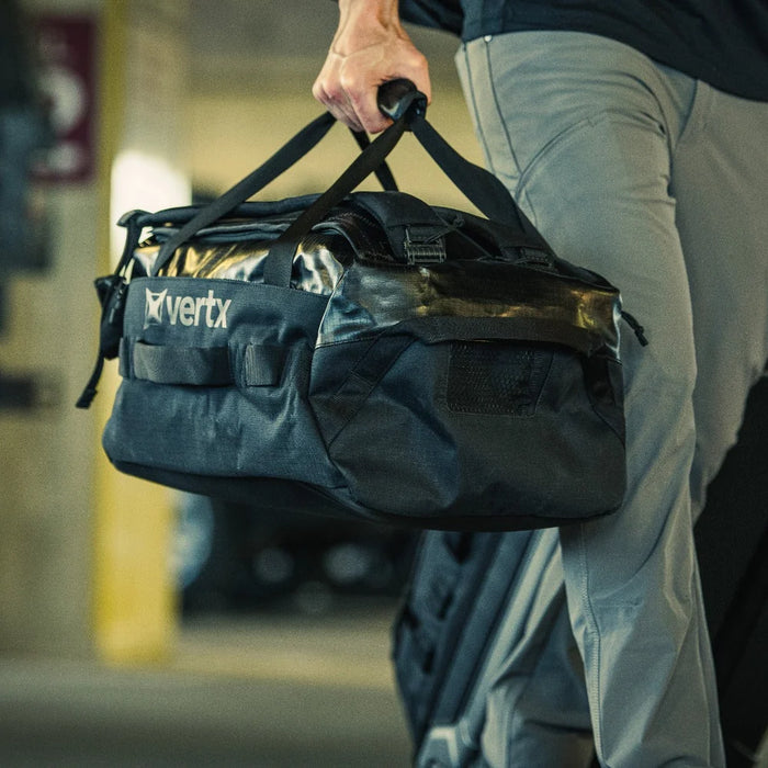 A traveler carries his black RLT 80L Duffel Backpack through an airport parking lot, utilizing the padded shoulder straps for a comfortable hands-free carry as he heads toward the terminal for his flight.