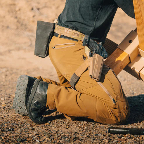 A shooter crouching comfortably in Eberlestock Deadwood Pants, utilizing the built-in knee pockets with neoprene inserts for protection and stability on uneven ground.