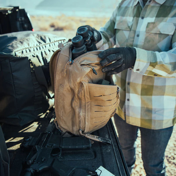 Shooter pulling binoculars from the soft tricot-lined top access zipper compartment of the Vertx Siege 15L Sling Bag.