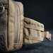 A side profile close-up of an olive green tactical bag, showing the reinforced nylon straps and side molle attachment points used for securing additional gear.