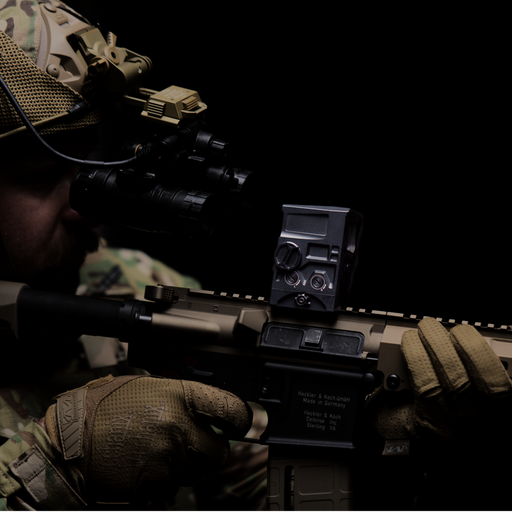 A side profile view of a tactical operator looking through the mounted DOT EHS-1 optic using helmet-mounted night vision goggles. The high mount provides proper clearance, demonstrating its effective use as a passive aiming NVG sight.