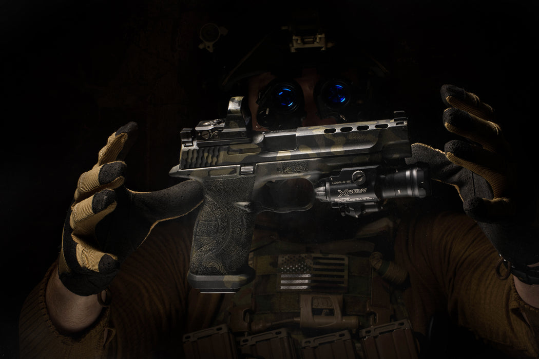 A profile shot of a tactical operator wearing night vision goggles, holding a handgun equipped with the SureFire X400VH LED White-Light & Infrared WeaponLight to demonstrate how the dual-spectrum beam integrates with head-mounted NODs.