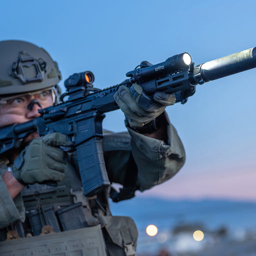 A tactical operator aims their rifle through an Aimpoint red dot sight, utilizing the Low-Profile Mount (LPM) to keep the weapon light tucked tightly against the handguard for a streamlined profile.