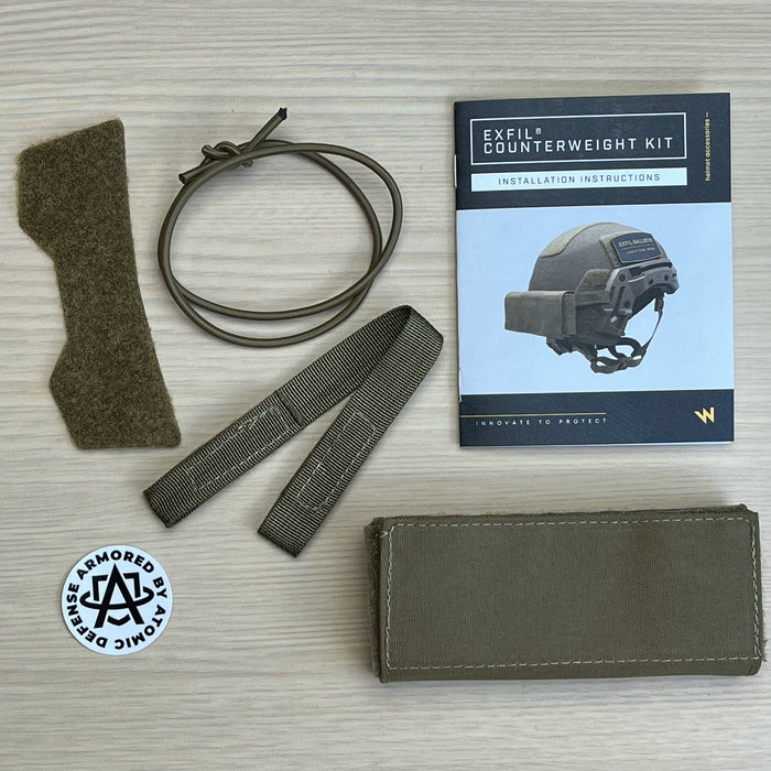 A top-down view of the team wendy counterweight kit contents, including the tactical weight pouch, three lead weights, attachment straps, and a bonus package of Atomic Defense stickers and candy.