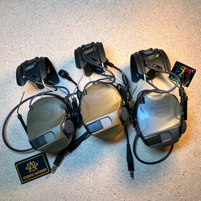Three rail-mounted 3M Peltor ComTac systems are displayed side-by-side to showcase the olive drab, coyote brown, and grey color variations of the ballistic headset accessories.