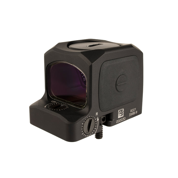 a right backside isometric product photo of the Trijicon RCR Red Dot Sight against a plain white background and prominently featured at the front-left, reflecting a dramatic green and orange dichroic coating and showing small white laser-engraved markings are visible along the base on the side saying '000030', 'RC01', and 'ISA 58:8'. At the base-front, another adjustment dial and 'UP' text with directional arrows are visible, and a short portion of a black mounting screw extends from the rear. 
