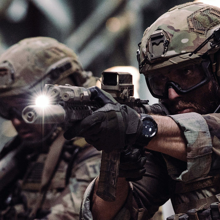 two members of a special forces unit are shown aiming rifles equipped with surefire scout light pro dual fuel, wearing tactical gear and helmets in what appears to be a training or operational environment