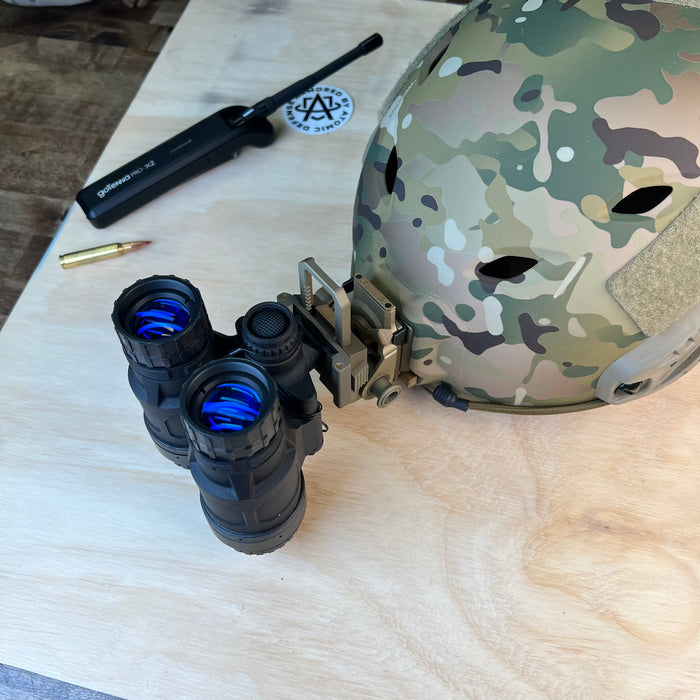 This profile view shows the Ultralight Articulating Night Vision Binocular in its stowed position, securely flipped up against a Team Wendy bump helmet. The device is attached via a Wilcox G24 mount, demonstrating how the compact housing sits low to the helmet shell to minimize snag hazards.