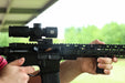 A side profile action shot of a black Cobalt Kinetics AR-15 firing, with a spent casing expelling from the chamber due to recoil. The rifle is equipped with a black Unity FAST Kickr mount, demonstrating its ability to maintain a steady 1.54-inch sight picture under heavy vibration.