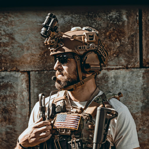 A side profile of a tactical operator wearing a Team Wendy EXFIL ballistic helmet with the unity mark team wendy adapter securely mounting 3M Peltor headsets to the side rails, while a Wilcox G24 mount holds a PVS-14 night vision monocular