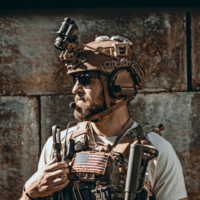 A side profile of a tactical operator wearing a Team Wendy EXFIL ballistic helmet with the unity mark team wendy adapter securely mounting 3M Peltor headsets to the side rails, while a Wilcox G24 mount holds a PVS-14 night vision monocular
