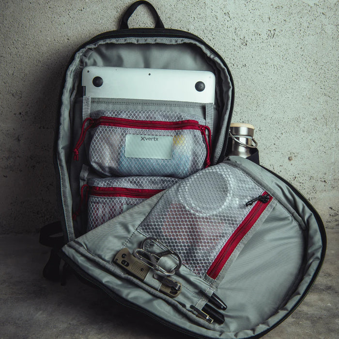 An interior shot of the Vertx Any Day 20L Backpack showing the main compartment unzipped to reveal various items organized within the 20-liter space and the high-visibility light-colored fabric that makes it easy to find gear in low light.