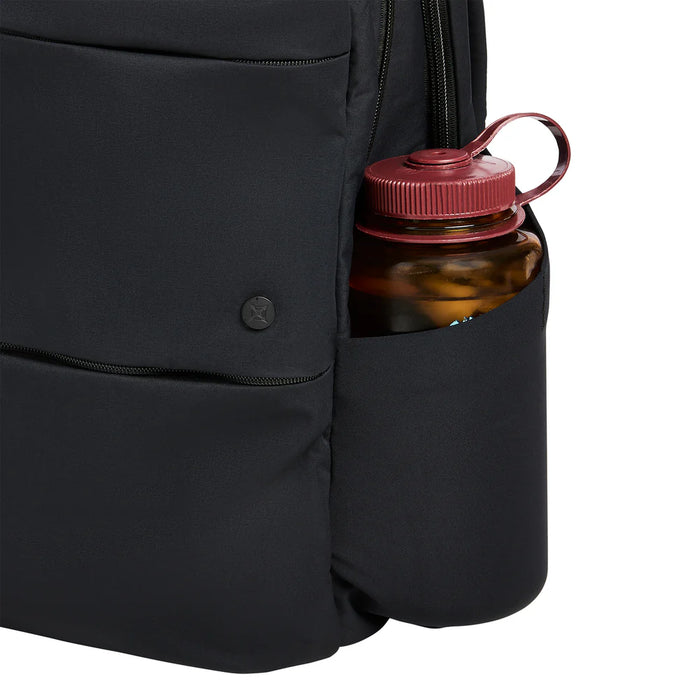 A close-up photograph of the stretch-woven side pocket on the Vertx Any Day 20L Backpack, showing its ability to securely hold a water bottle while maintaining a low profile when empty.