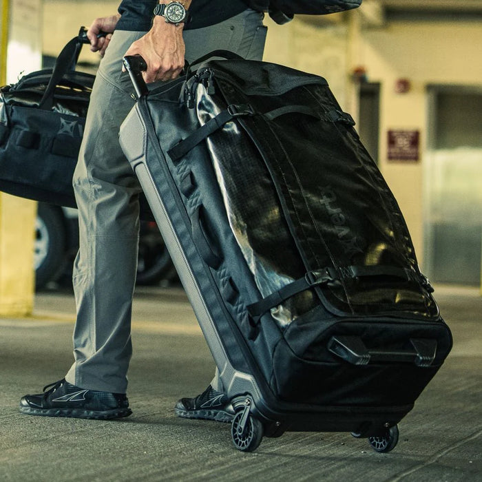 A traveler pulls the Vertx RLT 100L Duffel Roller through a parking garage, utilizing the aluminum retracting handle to tow his gear toward the terminal for a flight.